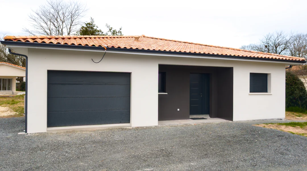 Petite maison en béton avec un garage attenant.